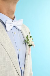 Photo of Groom in suit with stylish boutonniere on light blue background, closeup