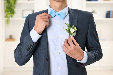 Photo of Groom in suit with stylish boutonniere indoors, closeup