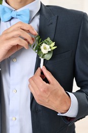 Photo of Groom in suit with stylish boutonniere indoors, closeup