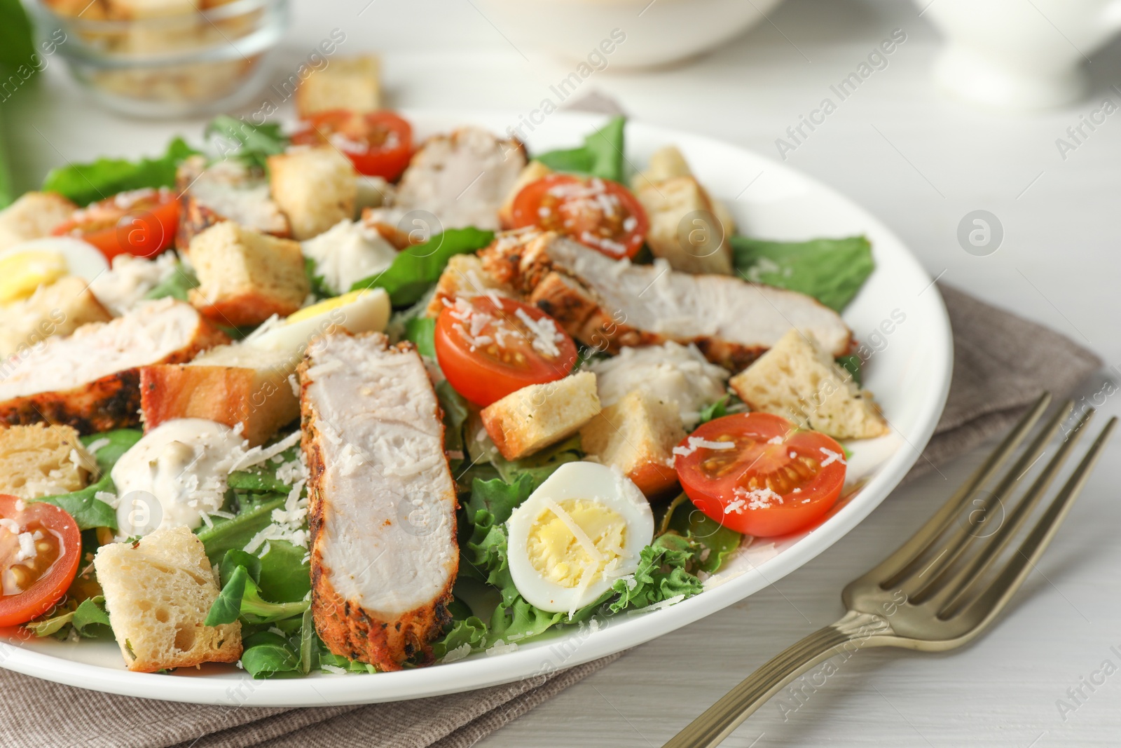 Photo of Tasty Caesar salad with chicken and tomatoes on white wooden table, closeup