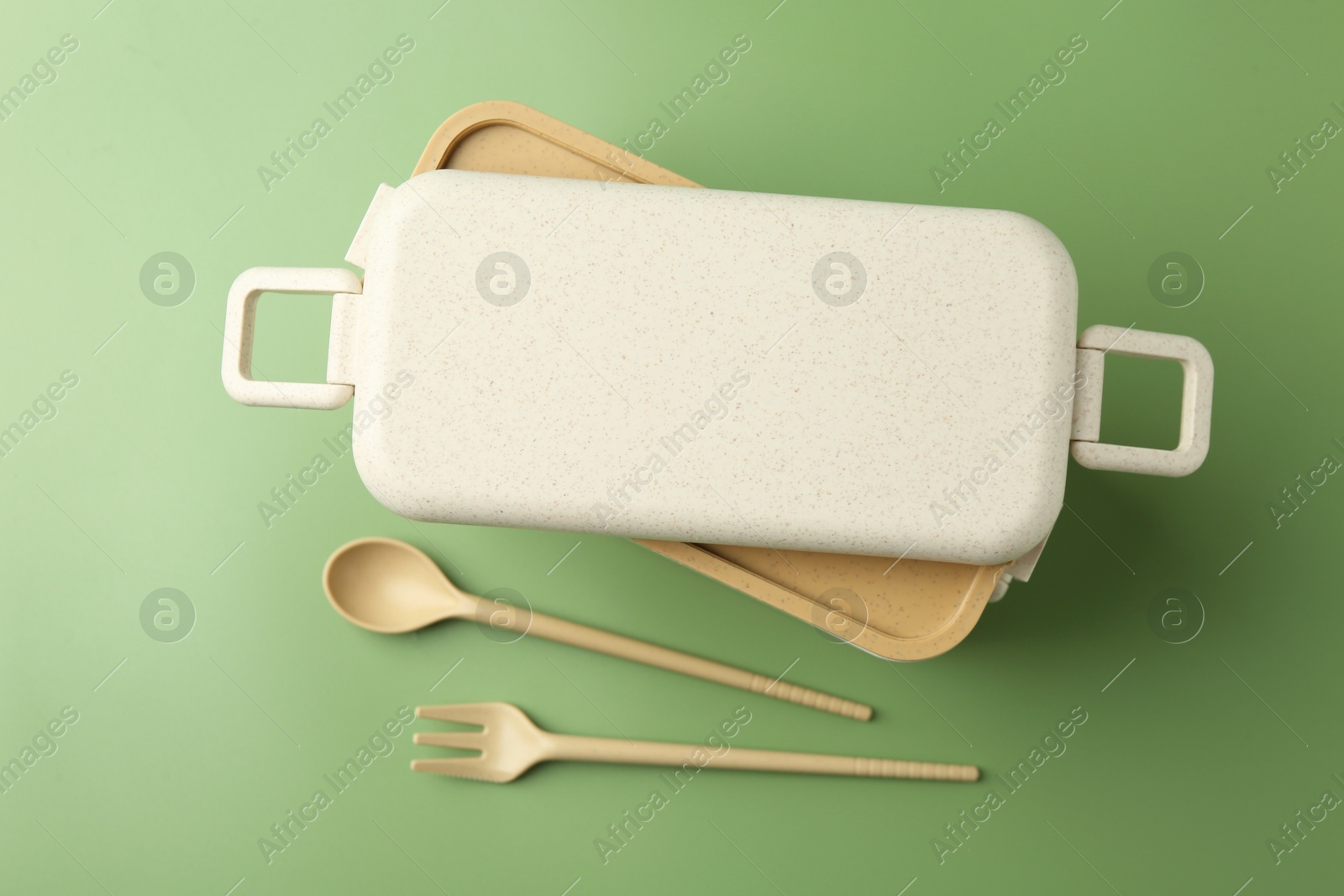 Photo of Plastic lunch box and cutlery on green background, flat lay