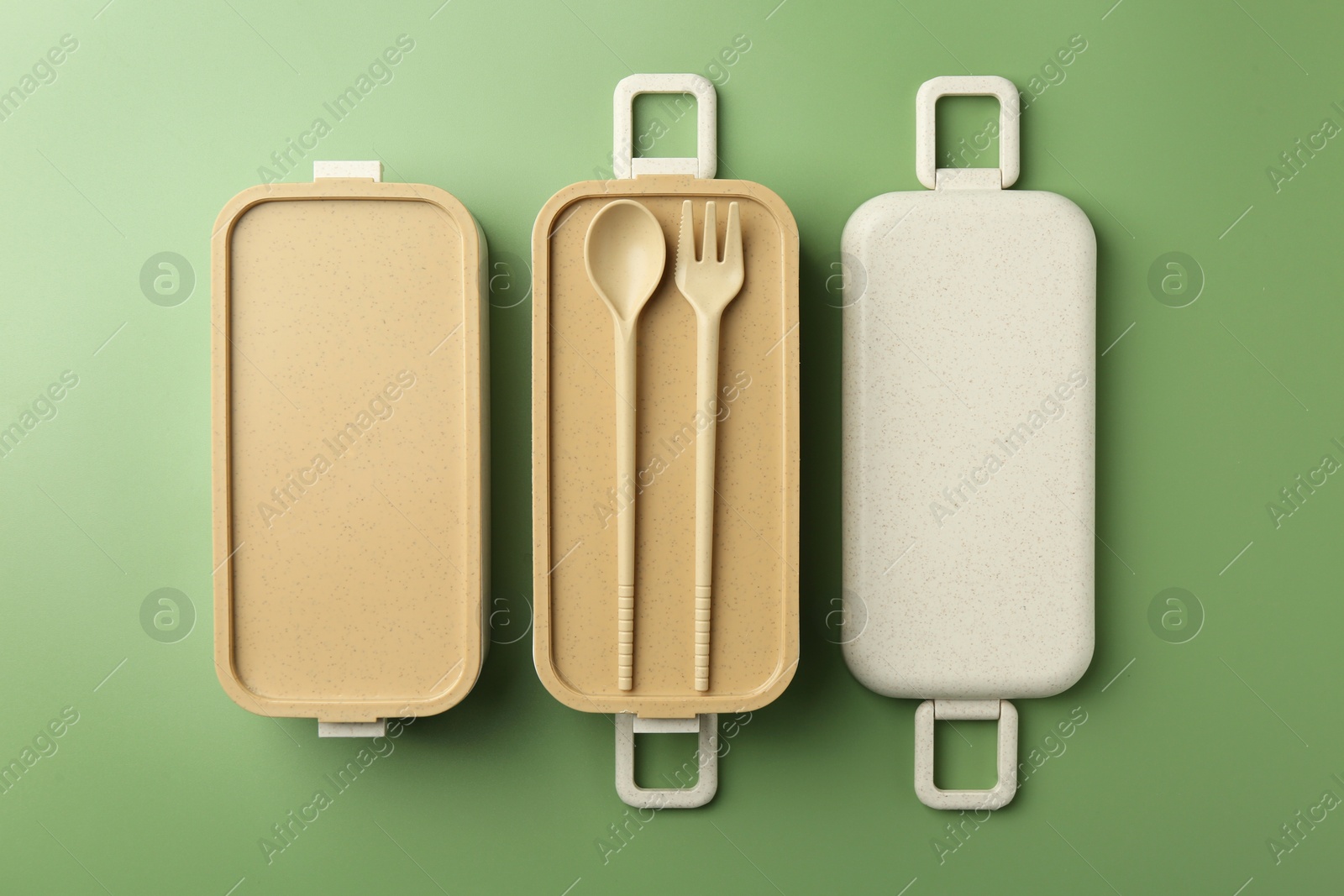 Photo of Compartments of plastic lunch box with cutlery on green background, flat lay