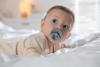 Photo of Cute little baby with pacifier on bed indoors