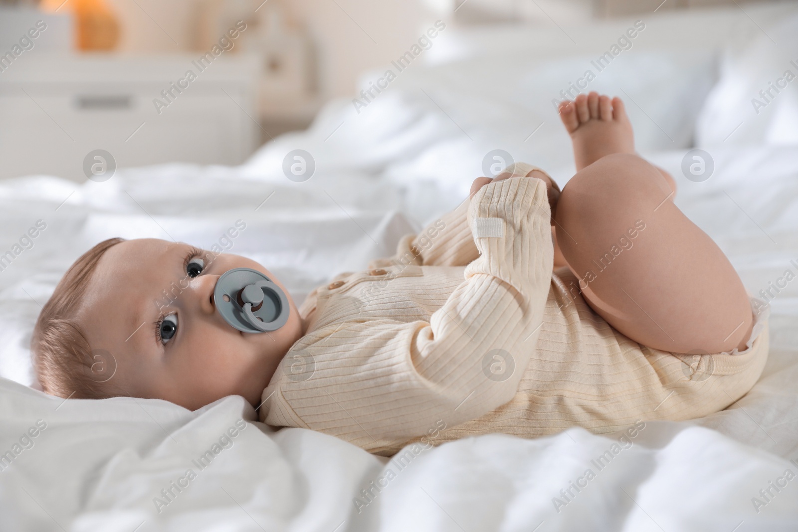 Photo of Cute little baby with pacifier on bed indoors