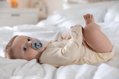 Cute little baby with pacifier on bed indoors