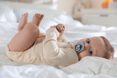 Cute little baby with pacifier on bed indoors