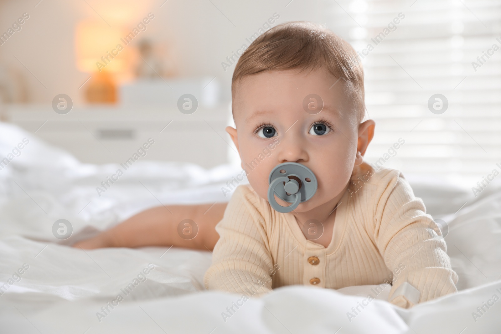 Photo of Cute little baby with pacifier on bed indoors