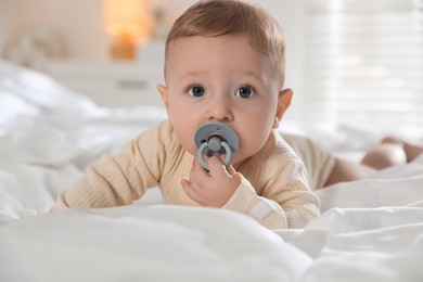 Photo of Cute little baby with pacifier on bed indoors