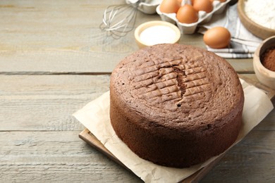 Photo of Tasty chocolate sponge cake and ingredients on wooden table, closeup. Space for text