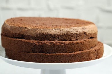 Photo of Cut chocolate sponge cake on stand against light background, closeup