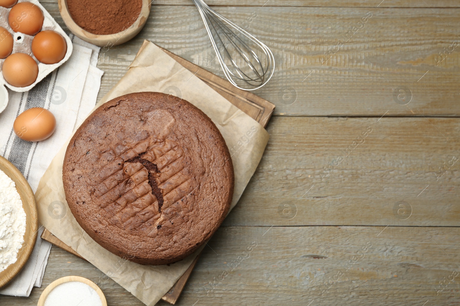 Photo of Tasty chocolate sponge cake and ingredients on wooden table, flat lay. Space for text