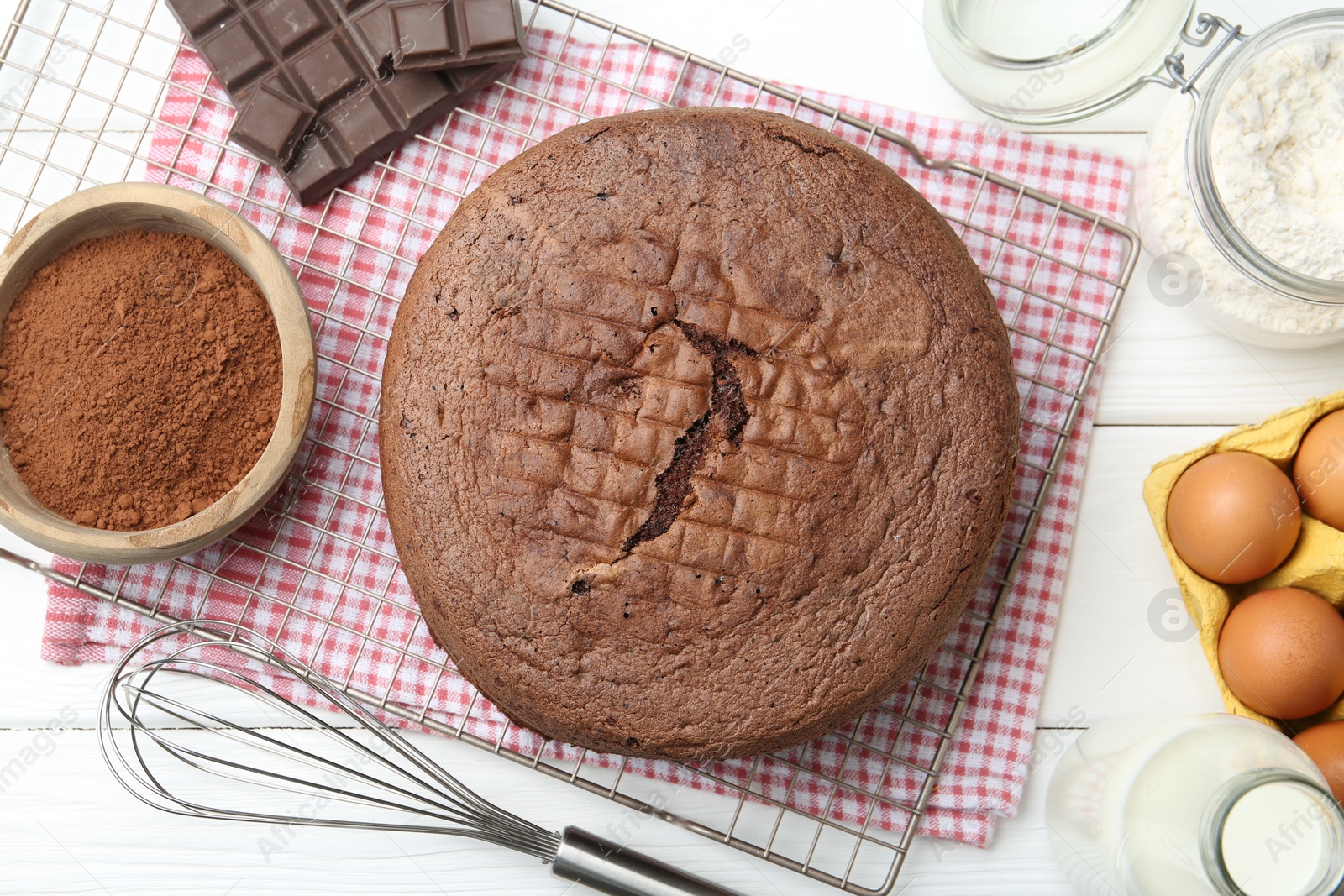 Photo of Tasty chocolate sponge cake, whisk and ingredients on white wooden table, flat lay