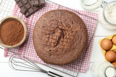 Photo of Tasty chocolate sponge cake, whisk and ingredients on white wooden table, flat lay