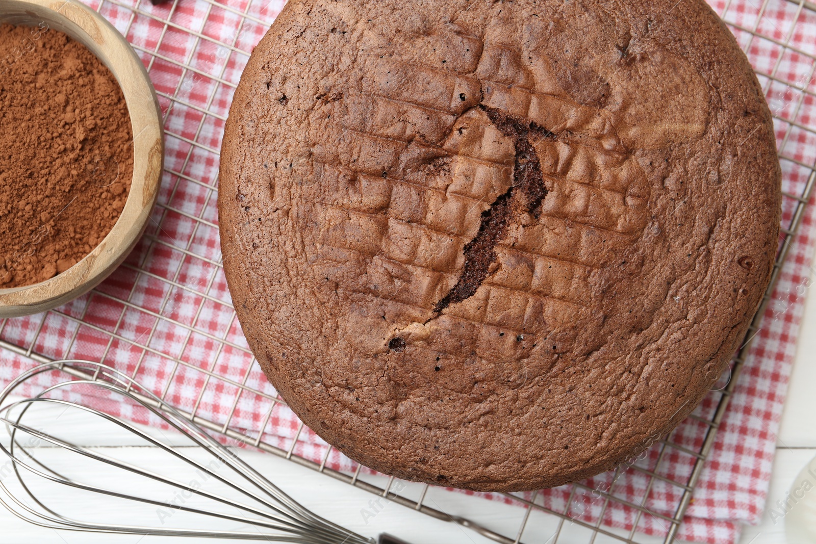 Photo of Tasty chocolate sponge cake, whisk and cocoa powder on white wooden table, top view