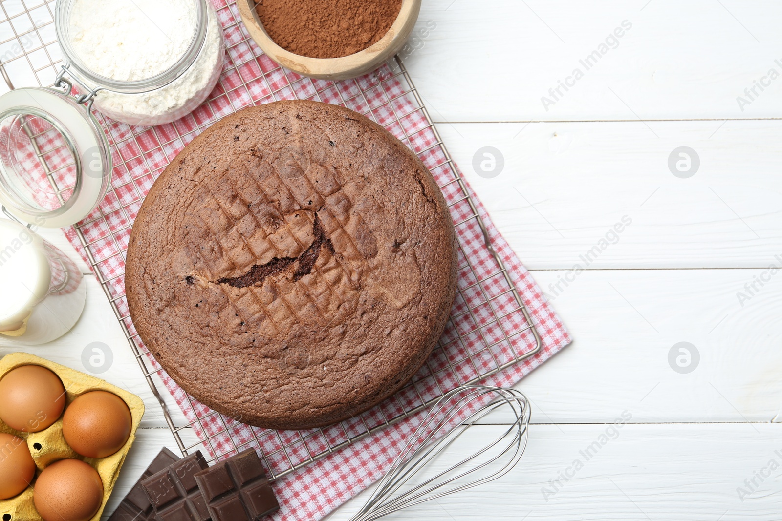 Photo of Tasty chocolate sponge cake, whisk and ingredients on white wooden table, flat lay. Space for text