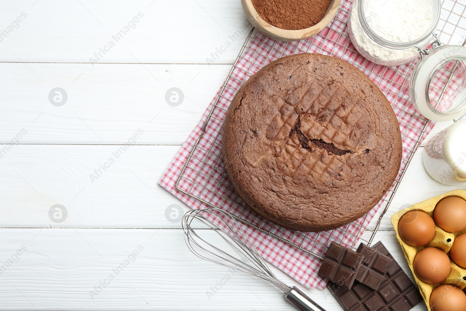 Photo of Tasty chocolate sponge cake, whisk and ingredients on white wooden table, flat lay. Space for text