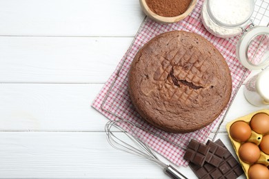 Photo of Tasty chocolate sponge cake, whisk and ingredients on white wooden table, flat lay. Space for text