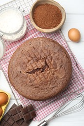 Photo of Tasty chocolate sponge cake, whisk and ingredients on white wooden table, flat lay