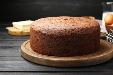 Photo of Tasty chocolate sponge cake and ingredients on black wooden table, closeup