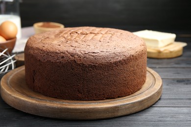 Photo of Tasty chocolate sponge cake and ingredients on black wooden table, closeup