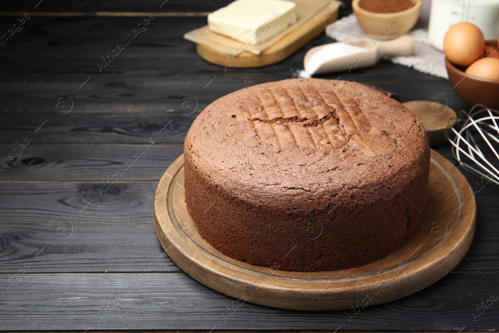 Photo of Tasty chocolate sponge cake and ingredients on black wooden table