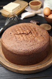 Photo of Tasty chocolate sponge cake and ingredients on black wooden table, closeup