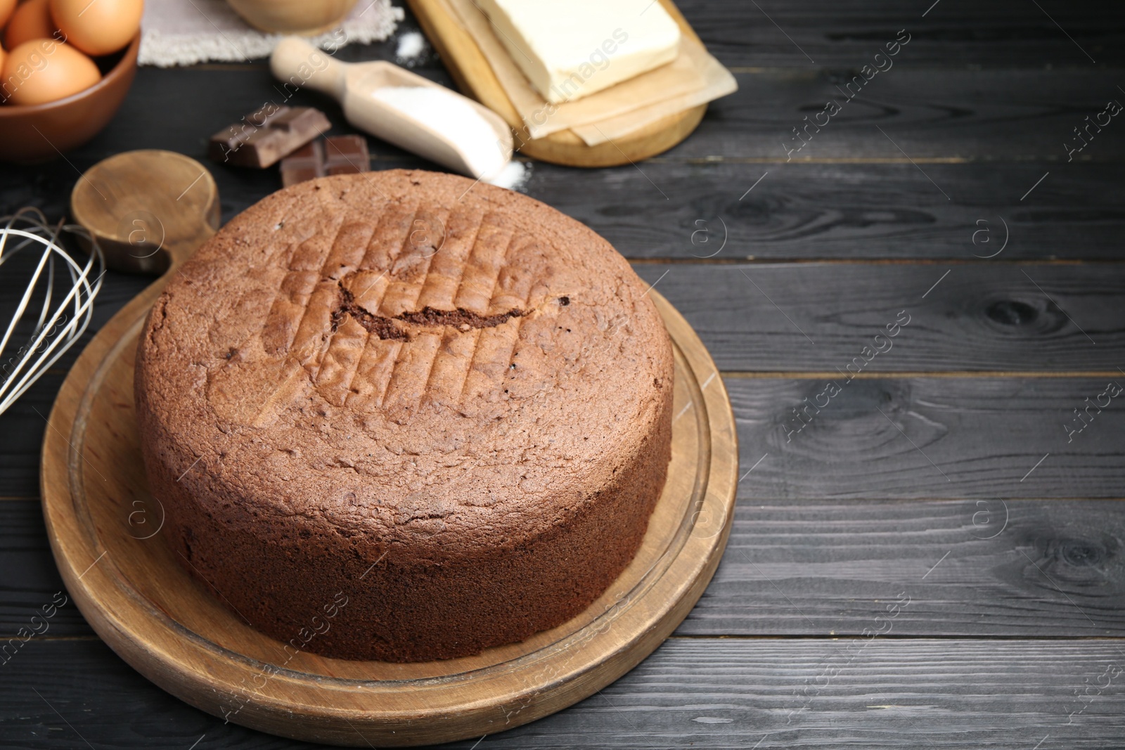 Photo of Tasty chocolate sponge cake and ingredients on black wooden table