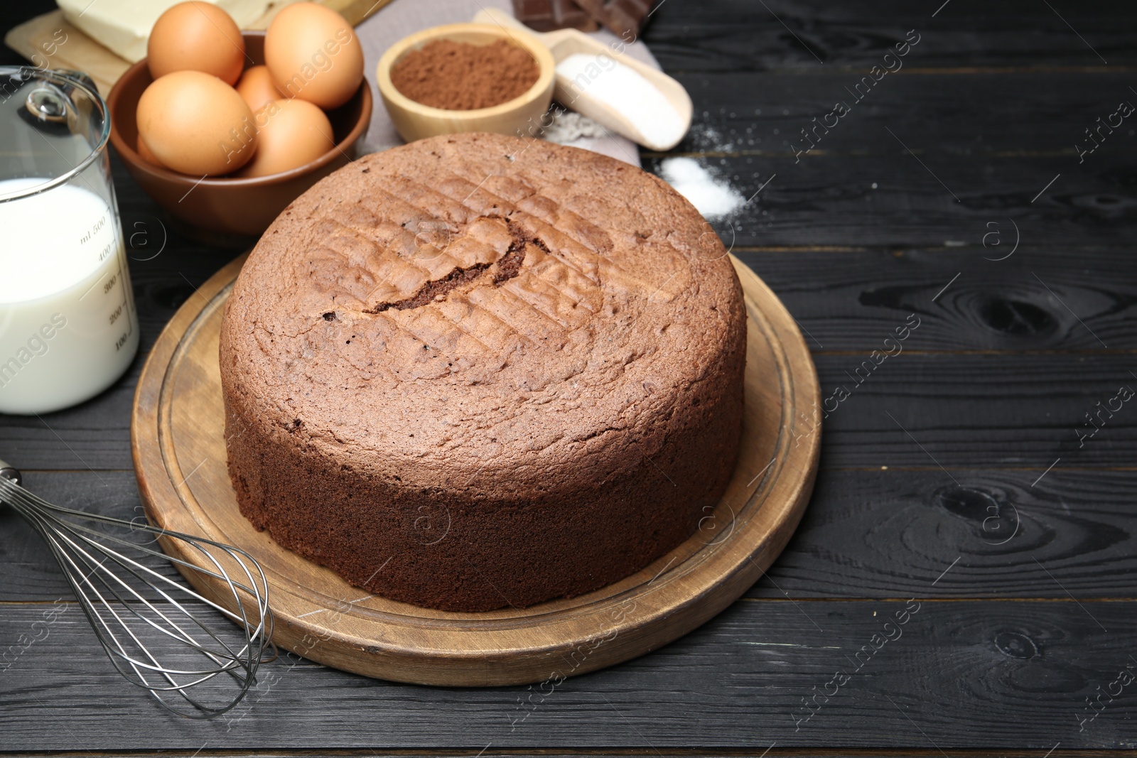 Photo of Tasty chocolate sponge cake and ingredients on black wooden table