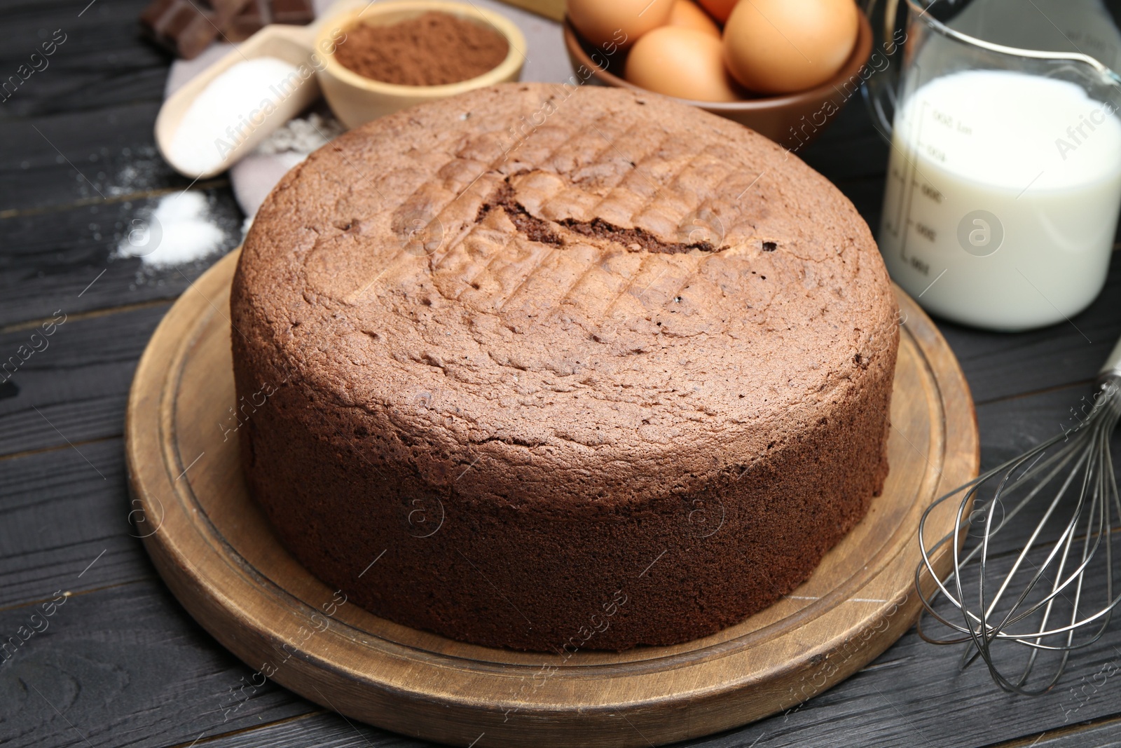 Photo of Tasty chocolate sponge cake and ingredients on black wooden table, closeup