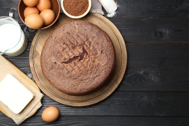 Photo of Tasty chocolate sponge cake and ingredients on black wooden table, flat lay. Space for text