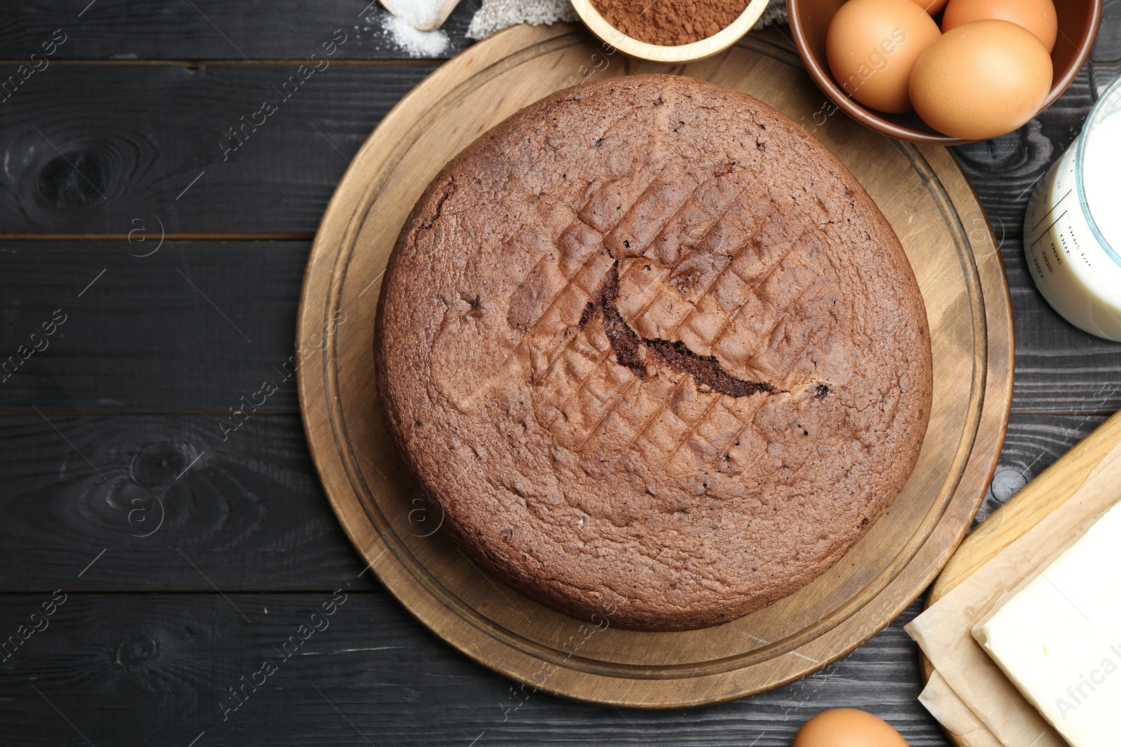 Photo of Tasty chocolate sponge cake and ingredients on black wooden table, flat lay