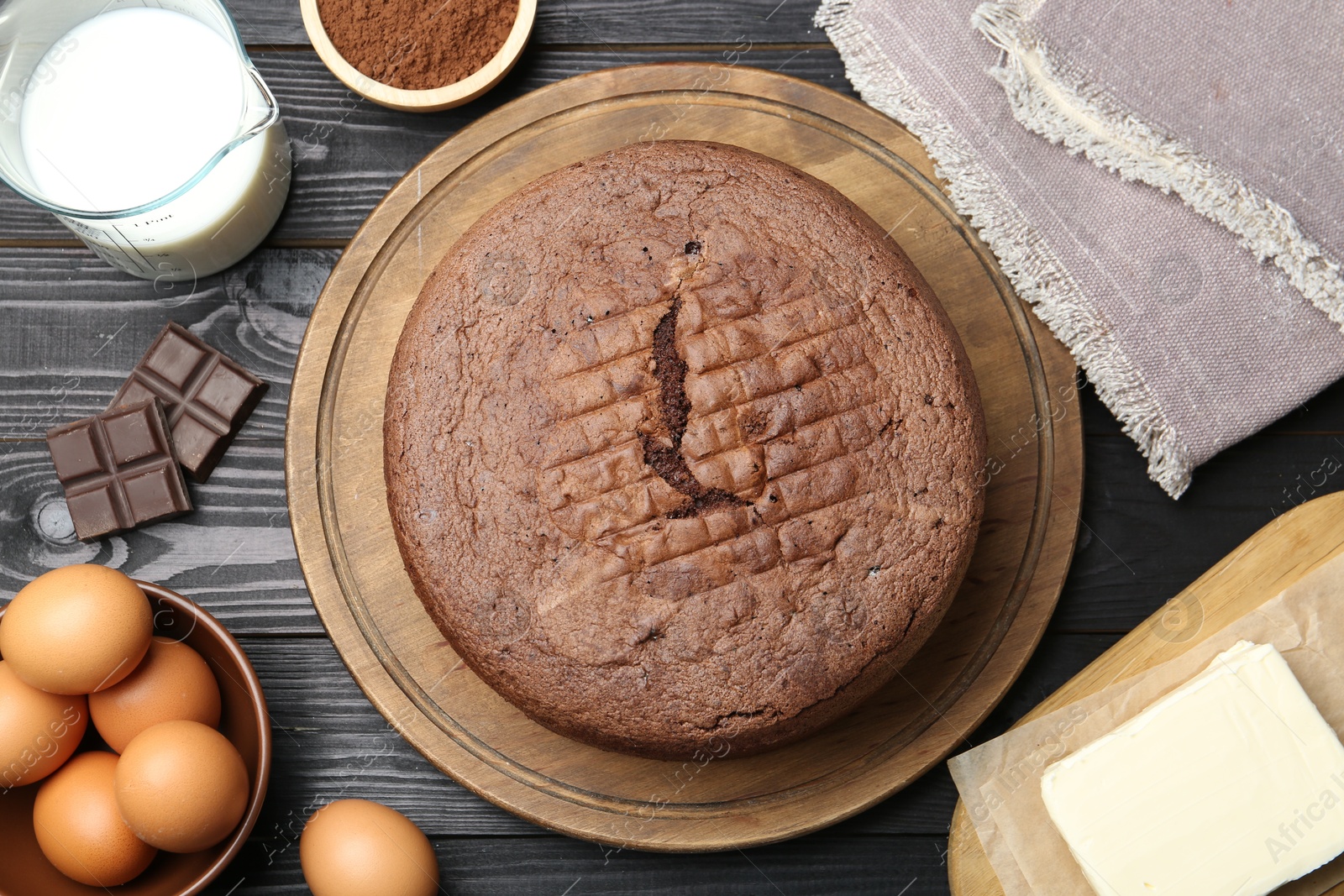 Photo of Tasty chocolate sponge cake and ingredients on black wooden table, flat lay