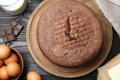 Photo of Tasty chocolate sponge cake and ingredients on black wooden table, flat lay