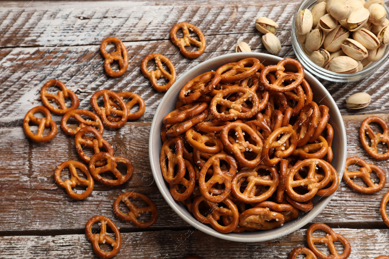 Photo of Delicious salty pretzel crackers and pistachios on wooden table, flat lay