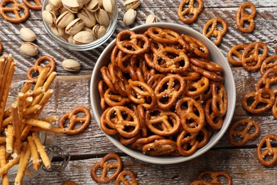 Photo of Delicious pretzel crackers, salty sticks and pistachios on wooden table, flat lay