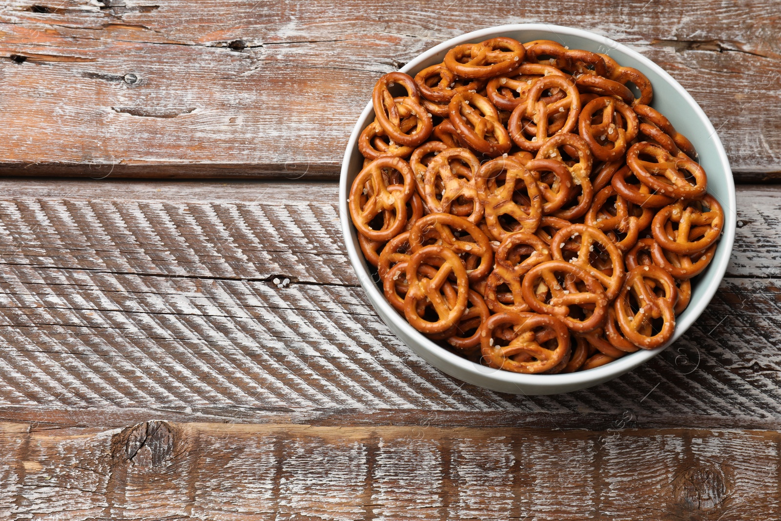 Photo of Delicious salty pretzel crackers on wooden table, above view. Space for text