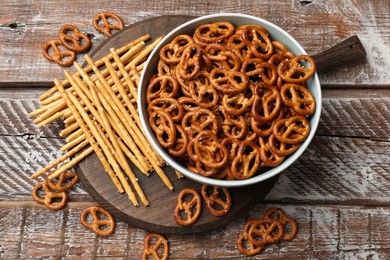 Photo of Delicious pretzel crackers and salty sticks on wooden table, flat lay