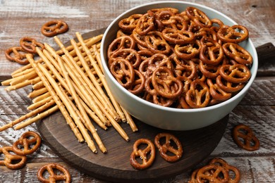 Photo of Delicious pretzel crackers and salty sticks on wooden table, closeup