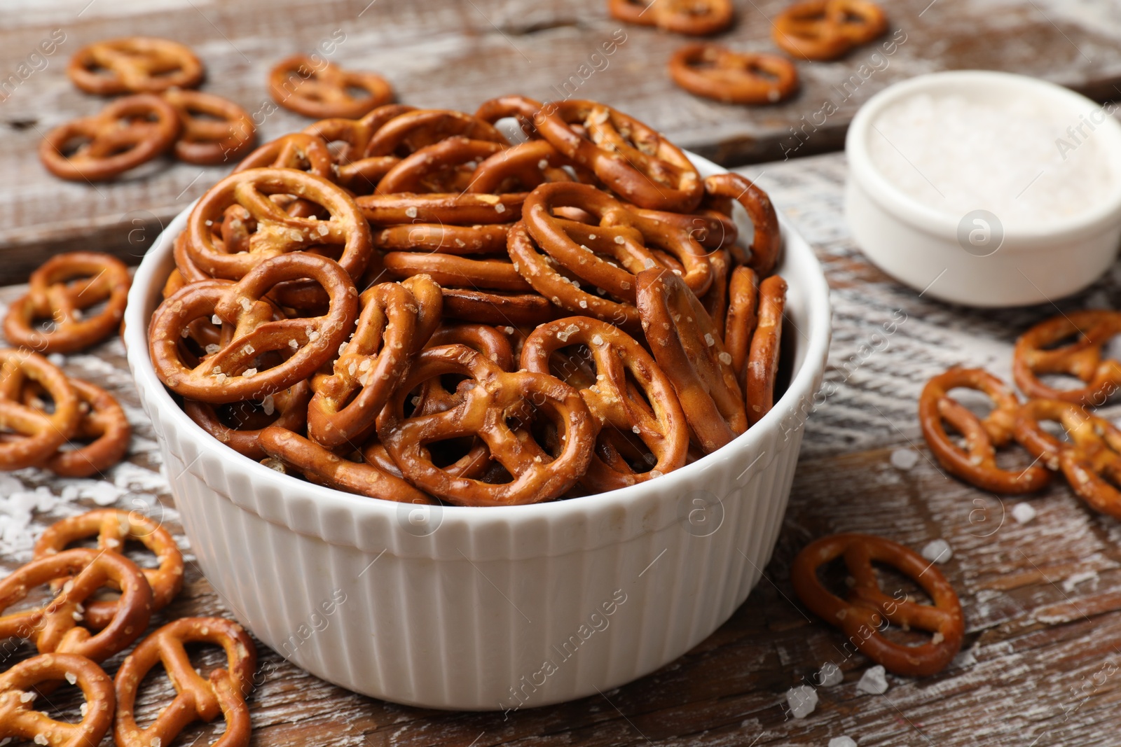 Photo of Delicious pretzel crackers and sea salt on wooden table, closeup