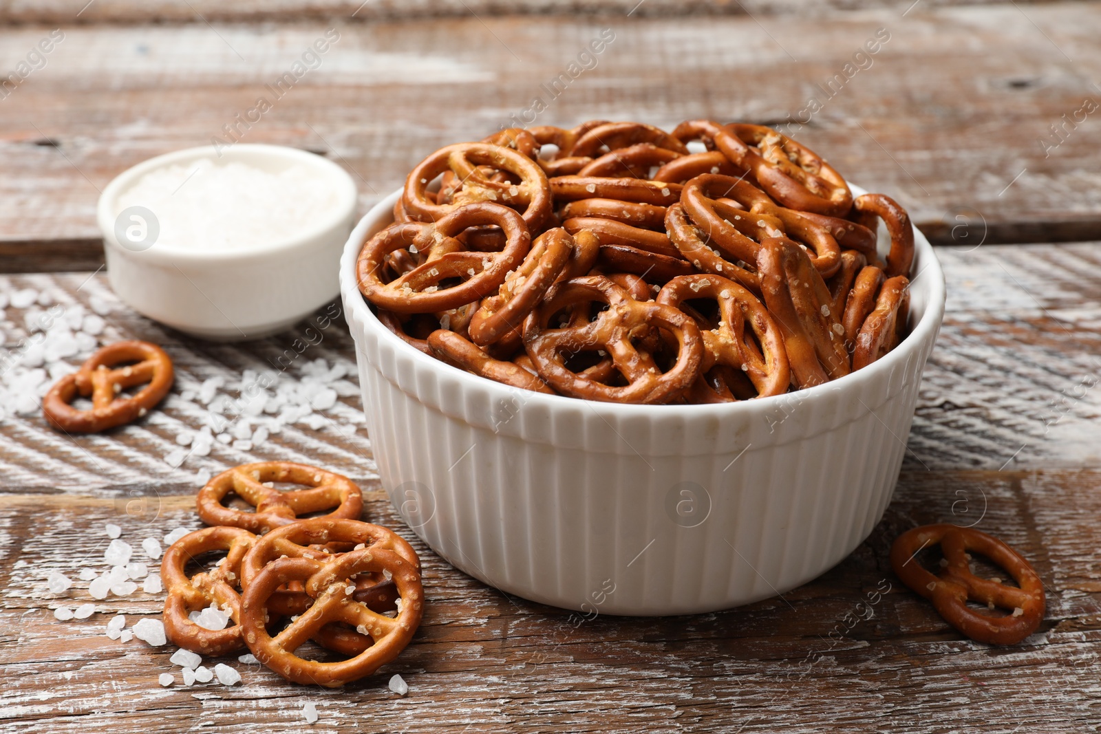 Photo of Delicious pretzel crackers and sea salt on wooden table, closeup