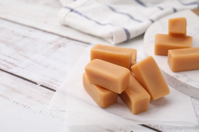 Photo of Tasty sweet caramel candies on white wooden table, closeup. Space for text