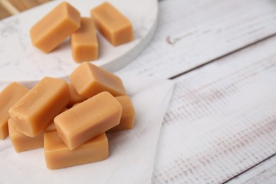 Photo of Tasty sweet caramel candies on white wooden table, closeup. Space for text