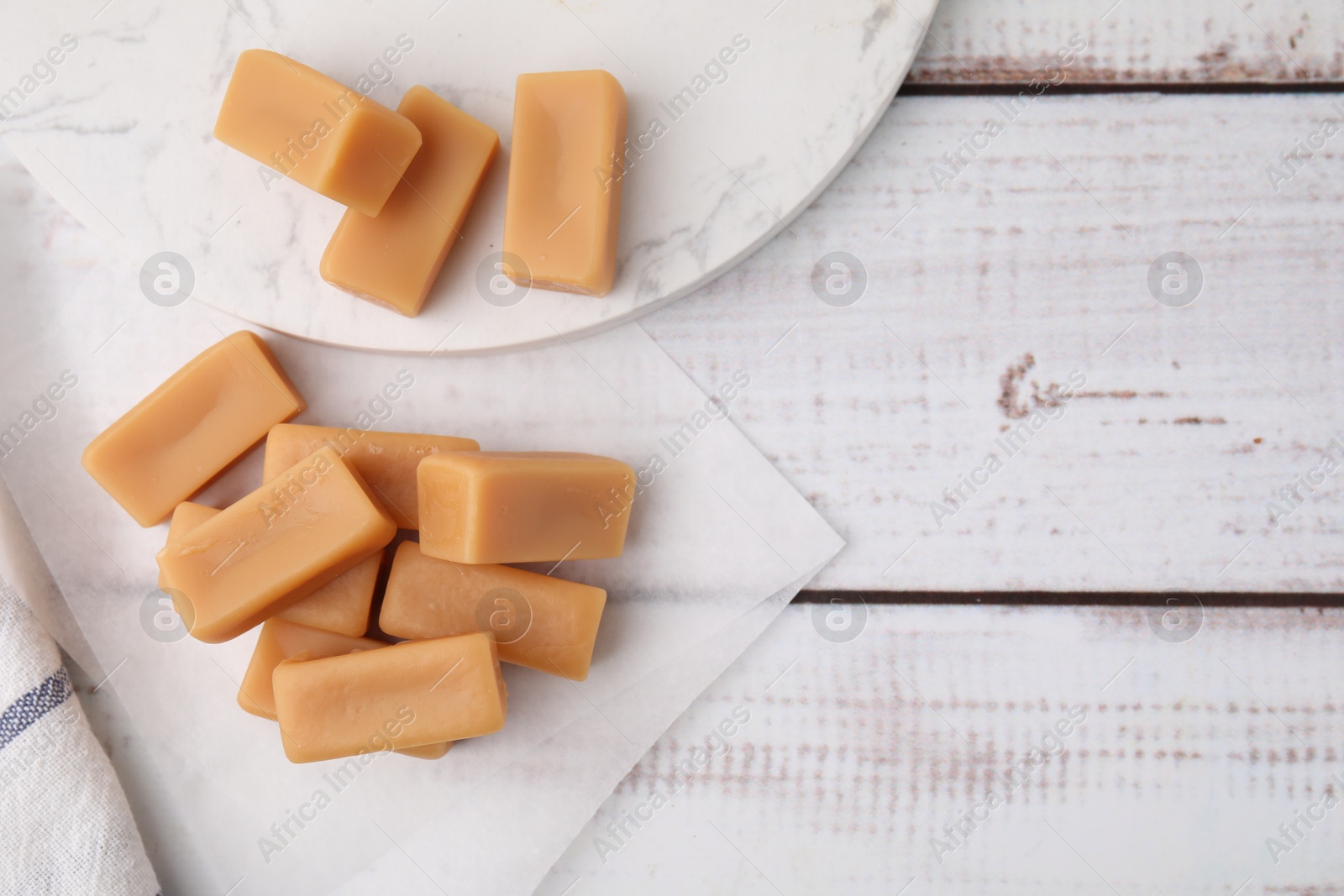 Photo of Tasty sweet caramel candies on white wooden table, flat lay. Space for text