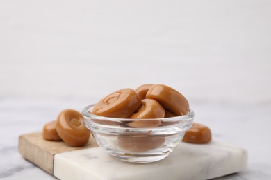 Photo of Tasty hard toffee candies in bowl on white table, closeup