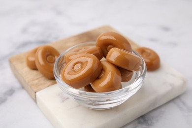 Photo of Tasty hard toffee candies in bowl on white marble table, closeup