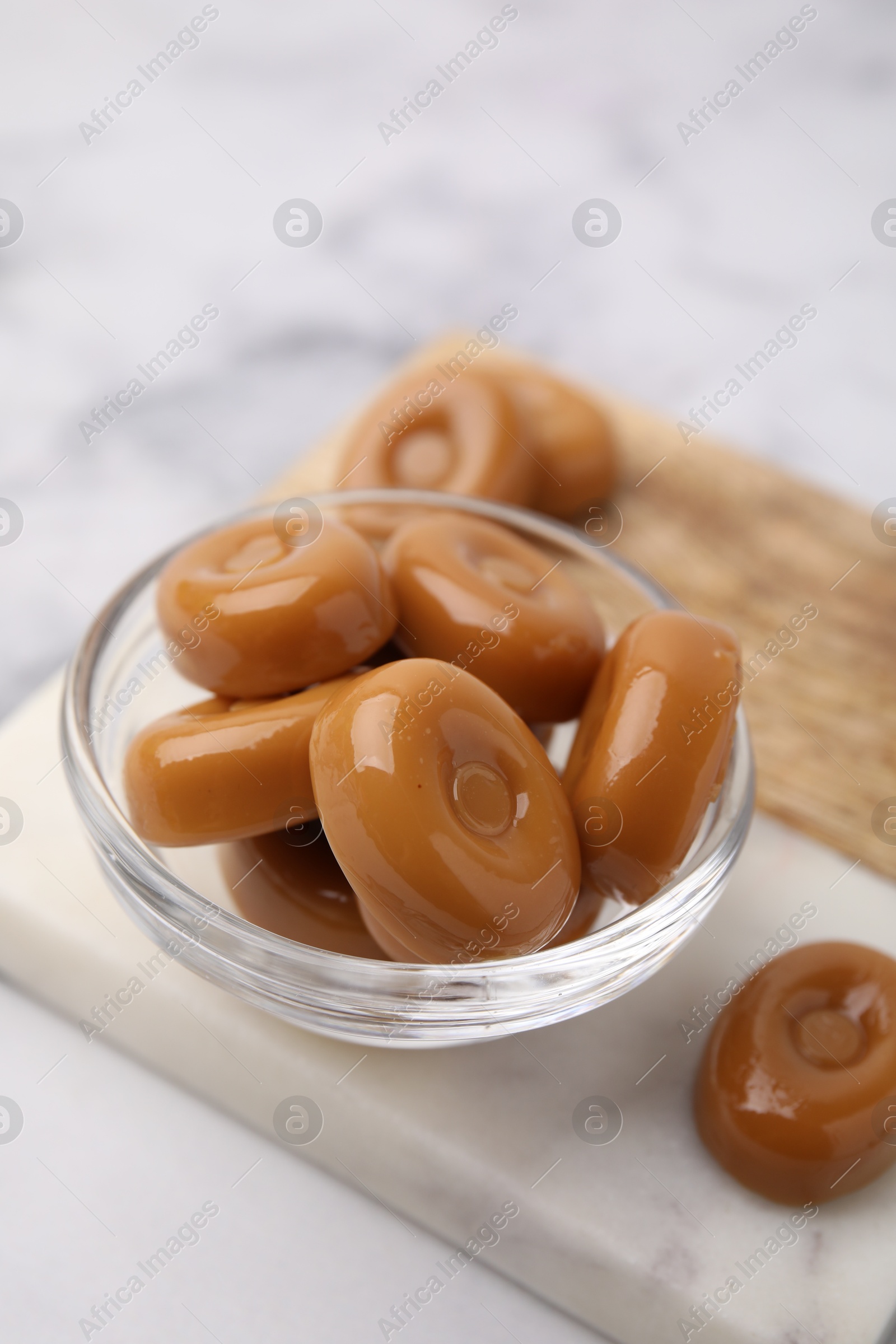 Photo of Tasty hard toffee candies in bowl on white marble table, closeup