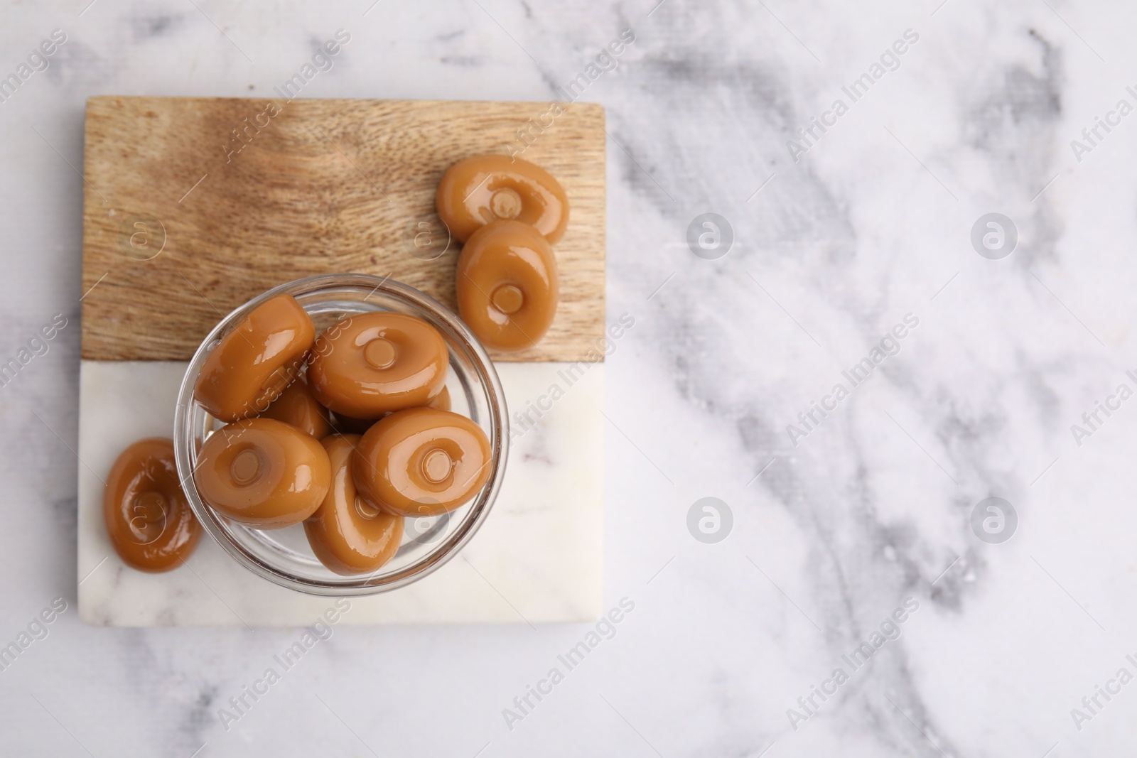 Photo of Tasty hard toffee candies on white marble table, top view. Space for text