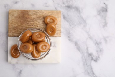 Photo of Tasty hard toffee candies on white marble table, top view. Space for text