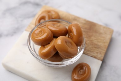 Photo of Tasty hard toffee candies in bowl on white marble table, closeup