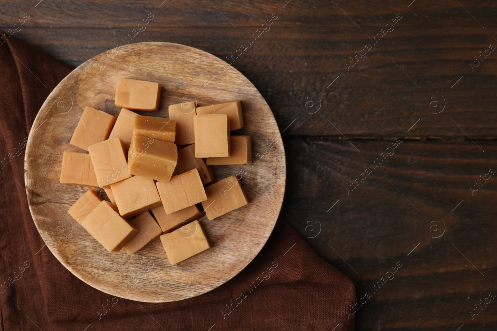 Photo of Tasty sweet caramel candies on wooden table, top view. Space for text